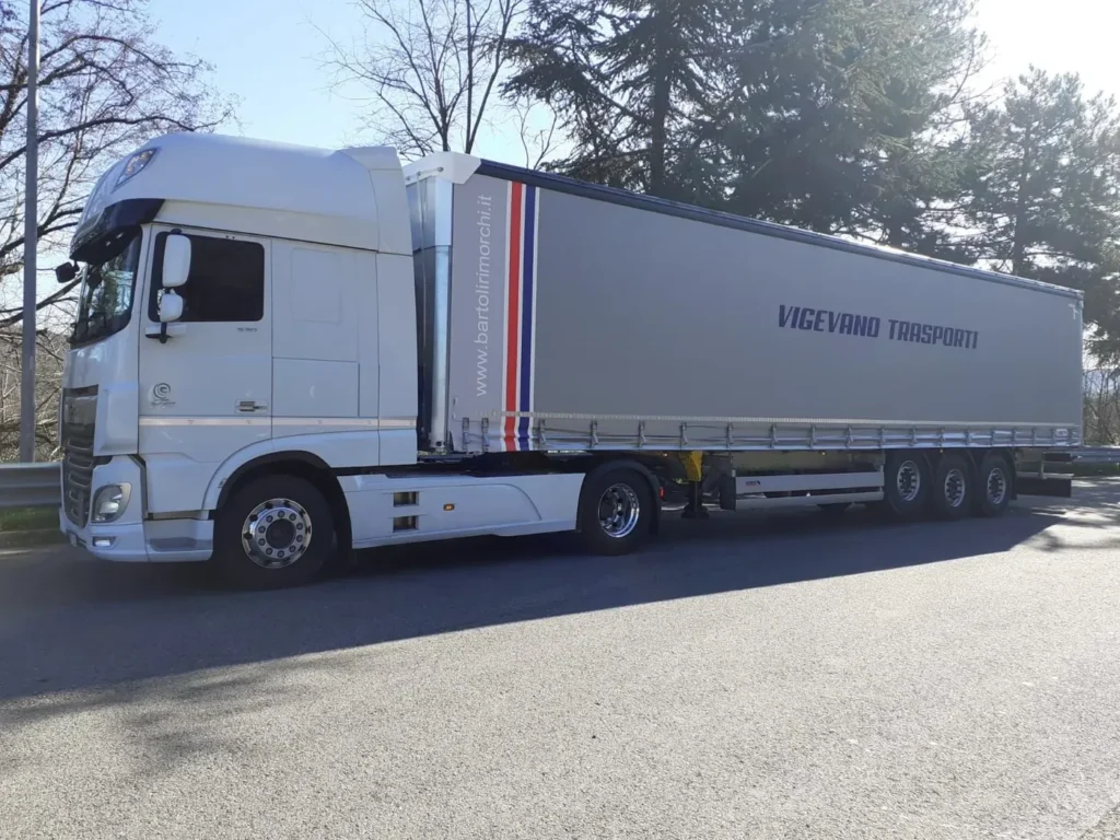 Camion bianco con semirimorchio centinato grigio fermo su un piazzale