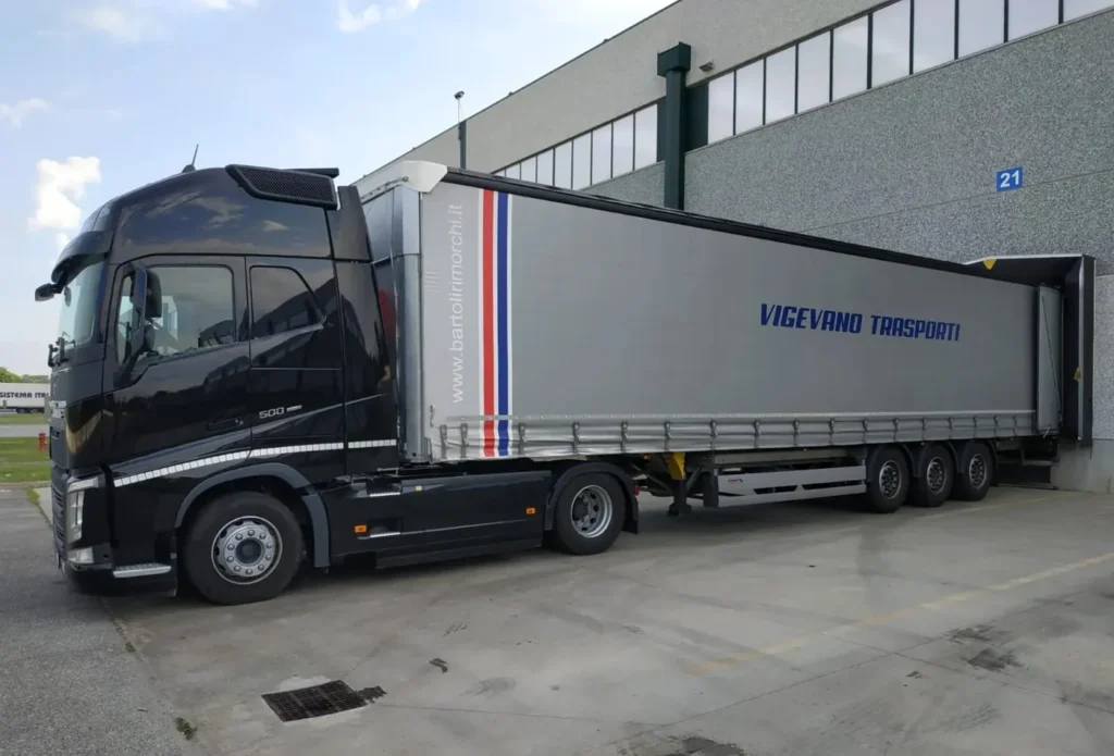 Camion Volvo nero con semirimorchio centinato fermo davanti a un magazzino