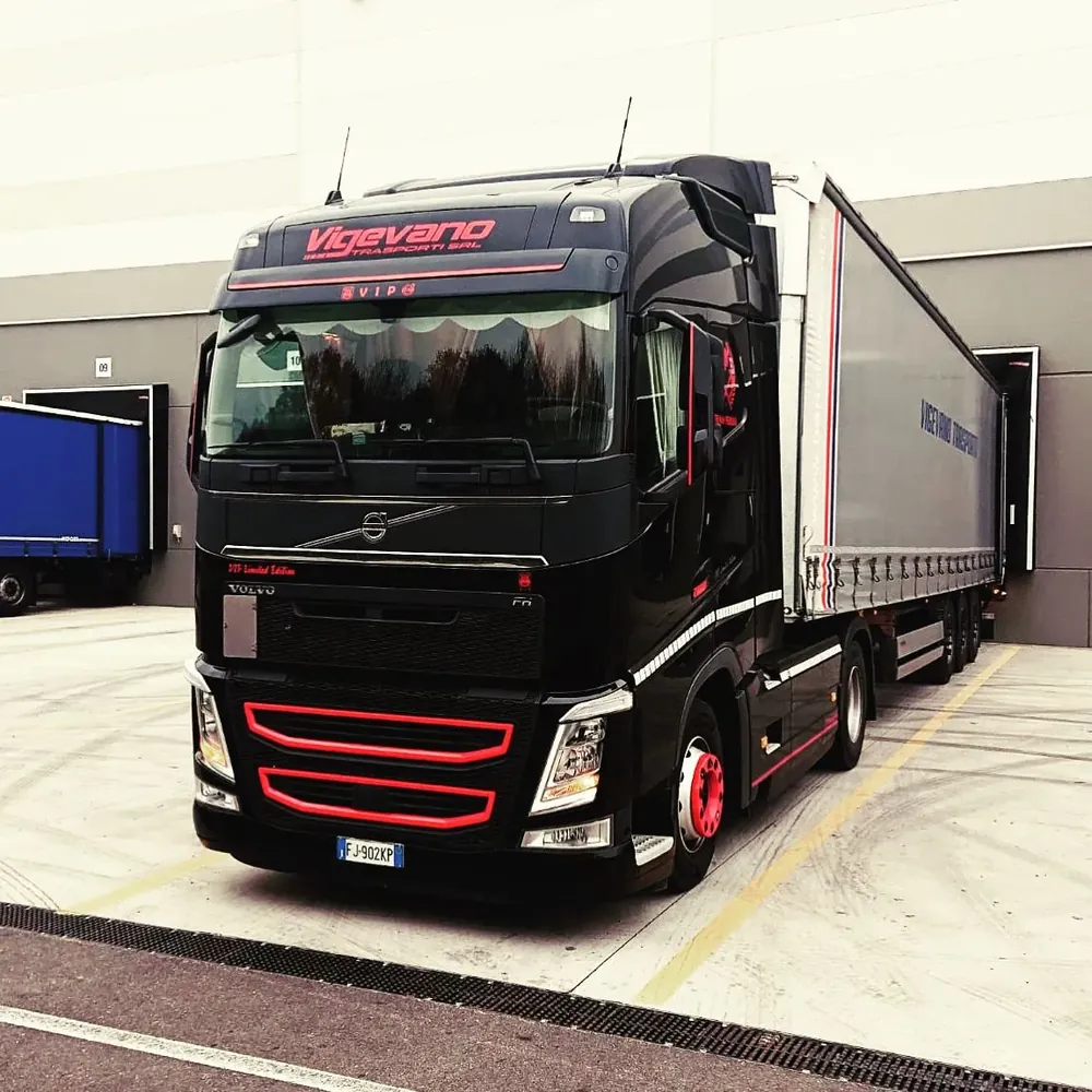 Parte anteriore di un camion Volvo nero con griglia rossa davanti a un magazzino