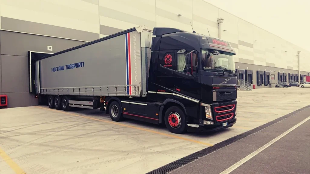 Camion nero Vigevano Trasporti con semirimorchio centinato davanti a una baia di carico